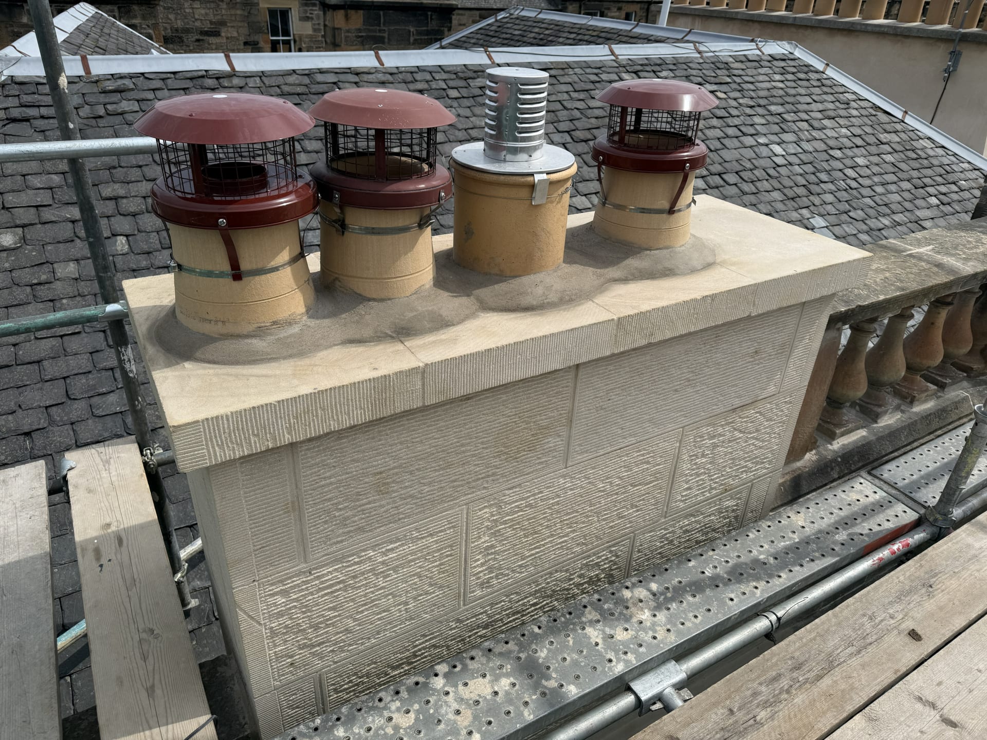 Rebuilt stone chimney stack with new chimney pots and cowls, surrounded by scaffolding